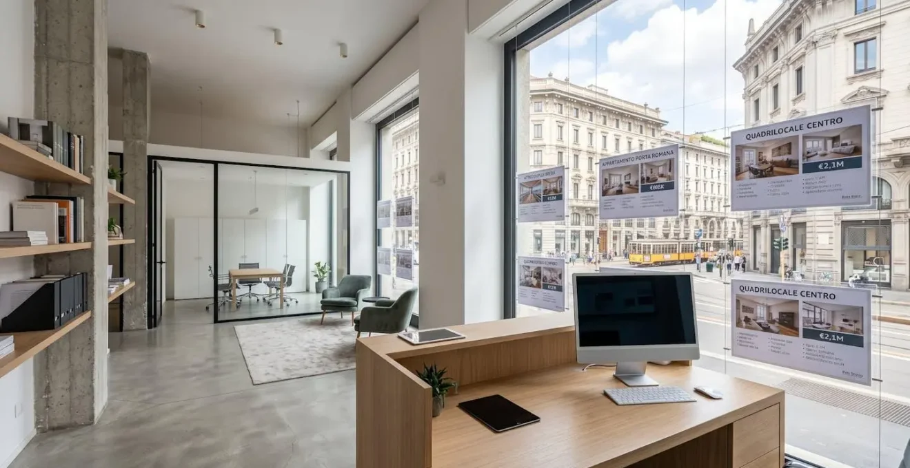 Veduta ampia dell'interno di un'agenzia immobiliare moderna a Milano, con scrivania pulita con monitor, annunci esposti in vetrina e abbondante luce naturale dalle ampie finestre, nessuna persona in primo piano